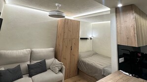 Un espace de vie moderne et compact comprenant un canapé, une petite table, un ventilateur de plafond et un lit.