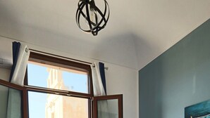 A hotel room with a bed, a view of the city, a balcony, and a painting on the wall. - LEVANZO Standard room with small private patio (Favignana)