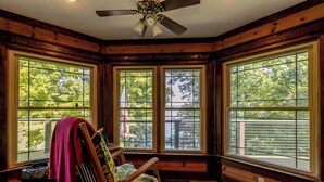 A cozy cabin interior with a rocking chair, large windows, and a ceiling fan. - Escape to our cozy lakeview cabin with modern amenities, spacious decks and serene surroundinngs. (Radford)