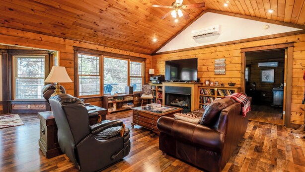 A cozy cabin interior with a fireplace, leather sofas, wooden floors, and a ceiling fan. - Escape to our cozy lakeview cabin with modern amenities, spacious decks and serene surroundinngs. (Radford)