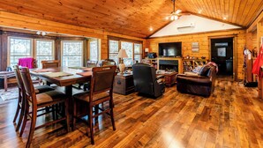 A spacious wooden cabin with a dining area, a living room with a fireplace, and a television. - Escape to our cozy lakeview cabin with modern amenities, spacious decks and serene surroundinngs. (Radford)