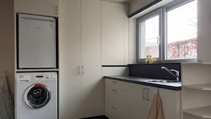 Ein kompakter Waschraum mit einer Waschmaschine von Bosch, einem Waschbecken und einem Fenster mit Blick auf Bäume.