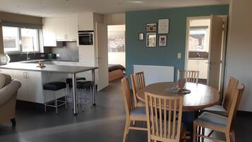 A modern kitchen with a central island, a dining area with wooden chairs, and a view of the city through the window.