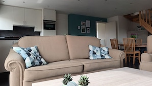 Ein modernes Wohnzimmer mit einem beigefarbenen Sofa, einem Holzesstisch und einer Treppe, die zu einer oberen Ebene führt.
