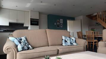 A modern living room with a beige sofa, a wooden dining table, and a staircase leading to an upper level.