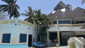 Un edificio de dos pisos con piscina, palmeras y un balcón con barandilla.