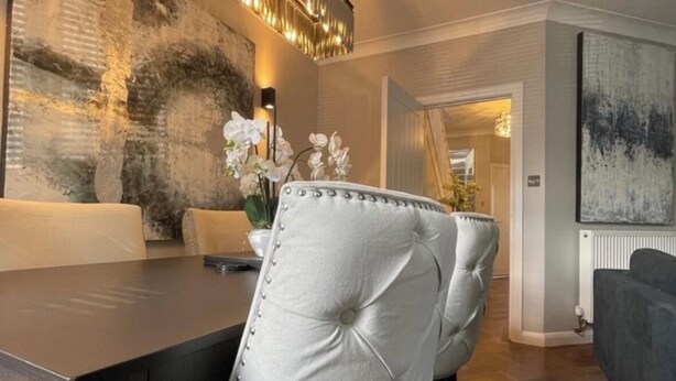 Un comedor moderno con una mesa de madera oscura, un sillón de cuero capitonado y un jarrón con flores blancas.