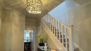 Un pasillo que conduce a una escalera con barandilla blanca y una consola decorativa con planta y vela.
