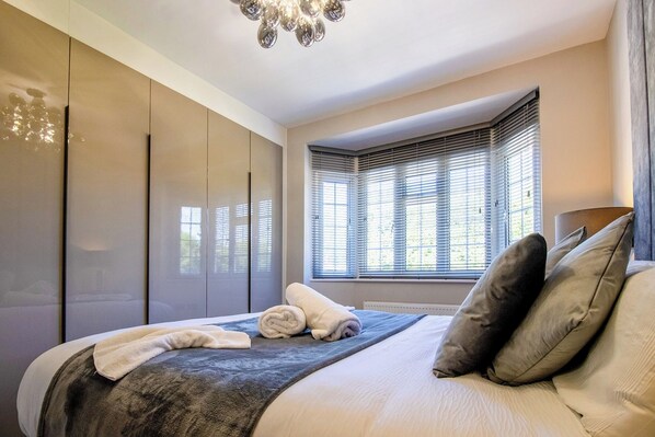 A bedroom with a large bed, a wardrobe, and a window with blinds.