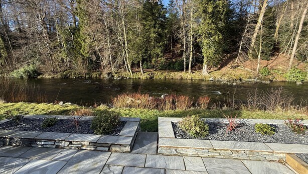 A stone deck with a river and forest in the background. - Greta House - Luxury refurbished accommodation (Central Keswick)