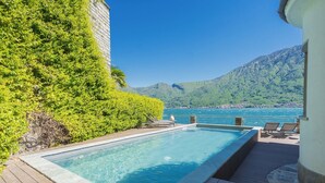 A rectangular swimming pool with a wooden deck, surrounded by lush greenery and a mountain backdrop. - Sala Comacina Villas by Rent all Como (Sala Comacina)