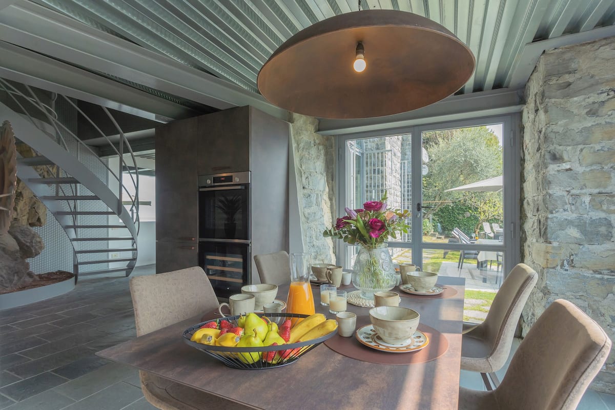 A dining area with a table set for breakfast, a fruit bowl, and a vase with flowers.