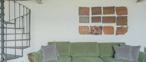 En grøn sofa med to puder, en spiraltrappe og en væg med ni strukturerede fliser.