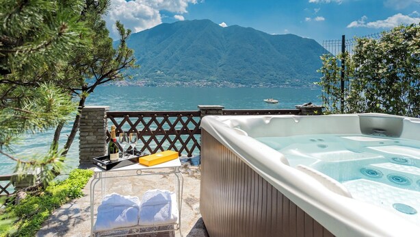 A hot tub with a mountain view, a stone table with bottles and glasses, and a wooden fence. - Sala Comacina Villas by Rent all Como (Sala Comacina)