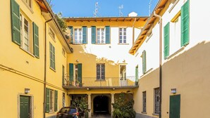 A narrow street with yellow buildings, green shutters, and a car parked at the entrance. - Rovelli 41 by Rent all Como (Como)