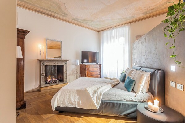 A bedroom with a bed, a fireplace, a television, and a large plant.