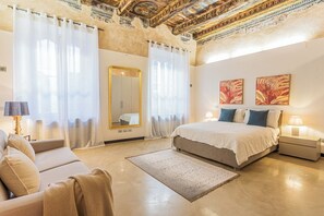 Ein geräumiges Schlafzimmer mit einem großen Bett, einer Sitzecke mit einer Couch und einem dekorativen Spiegel.