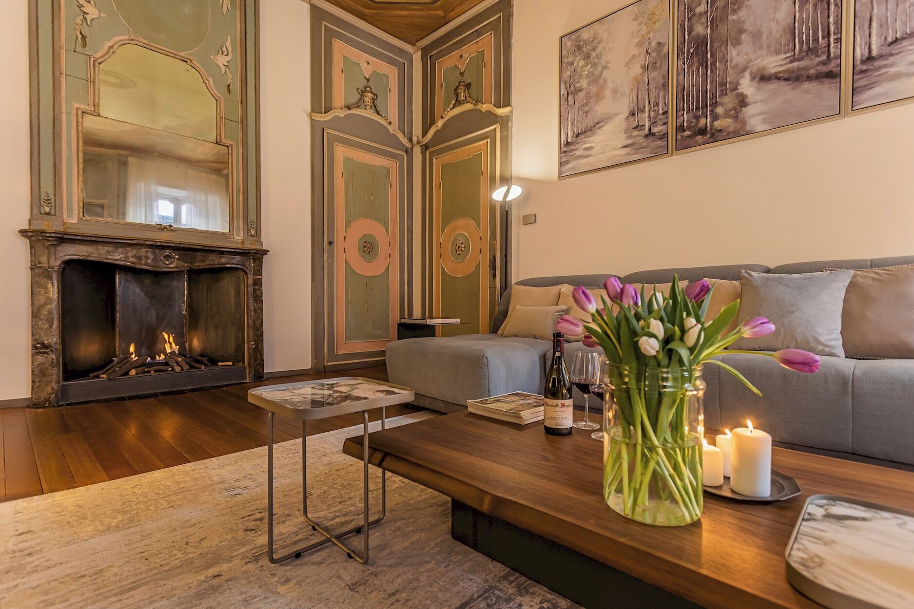 A living room with a fireplace, a sofa, a coffee table with a vase of flowers, and candles.