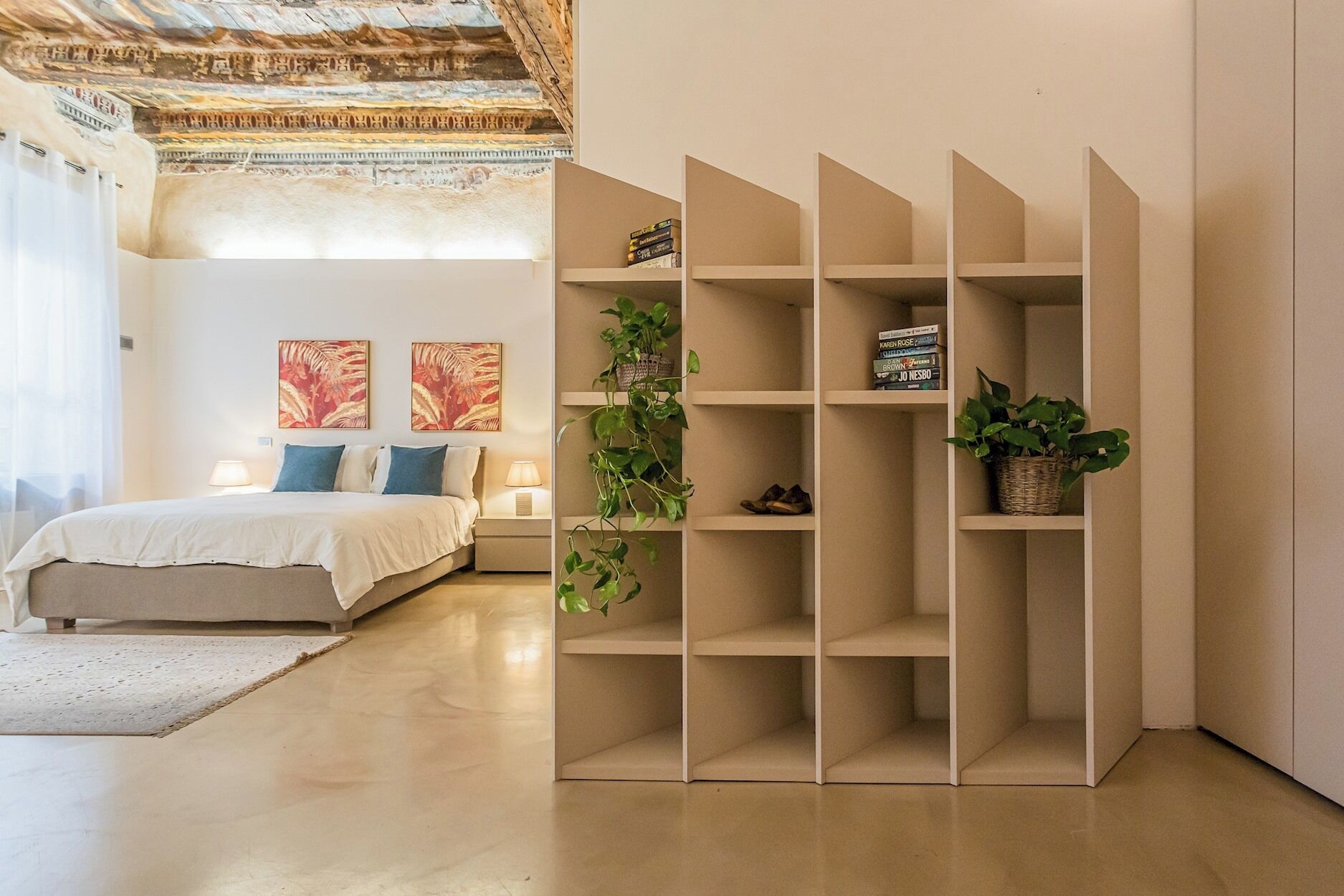 Un dormitorio con cama, mesitas de noche, una estantería y techo decorativo.