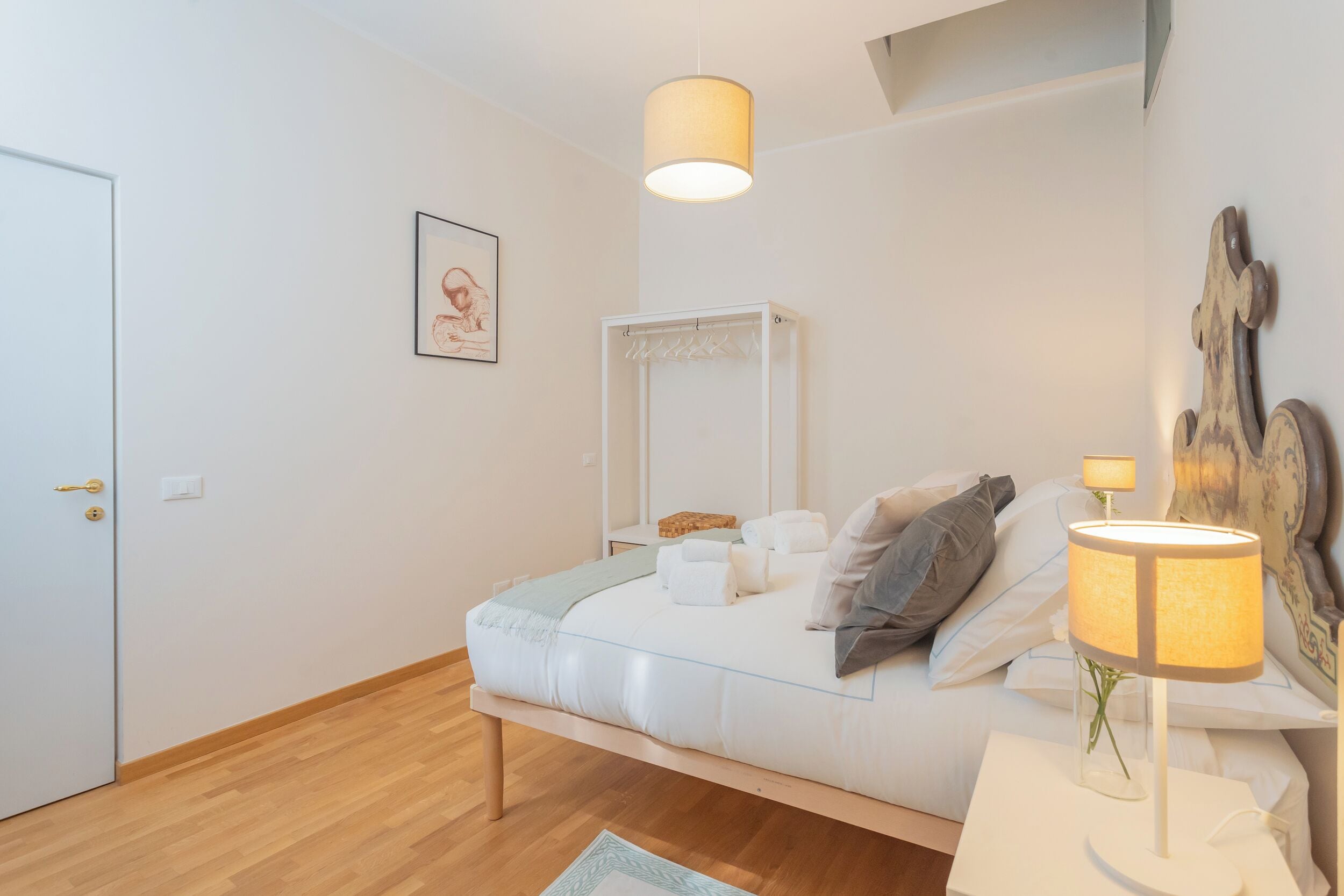 A bedroom with a bed, bedside table, lamp, and a mirror.
