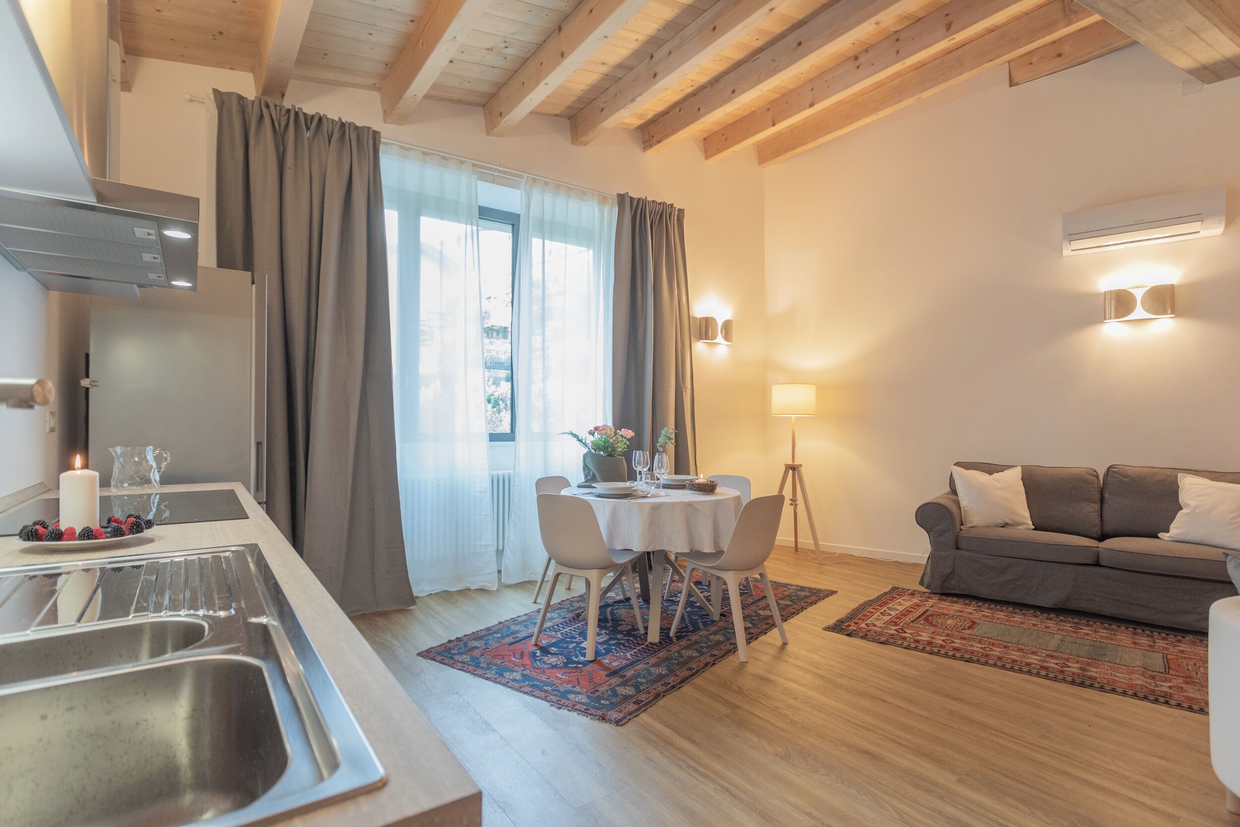Et moderne køkken med vask, spisebord med stole, en grå sofa og en mønstret måtte.