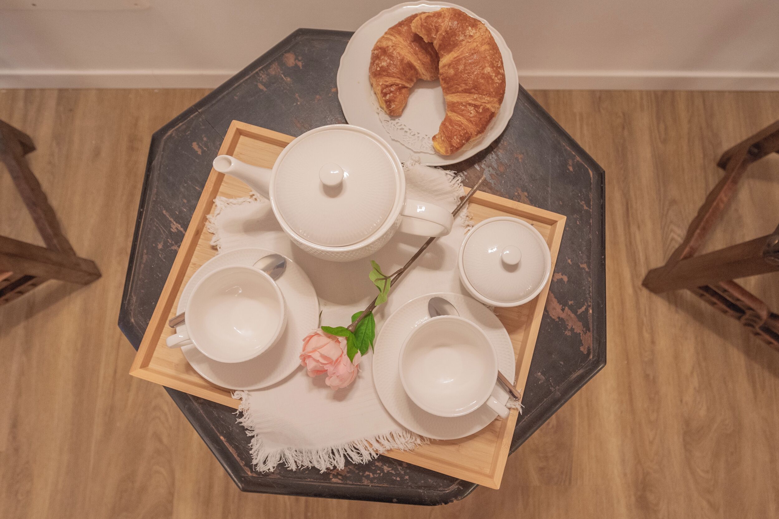 A breakfast tray with a croissant, teapot, cups, and saucers on a wooden table.