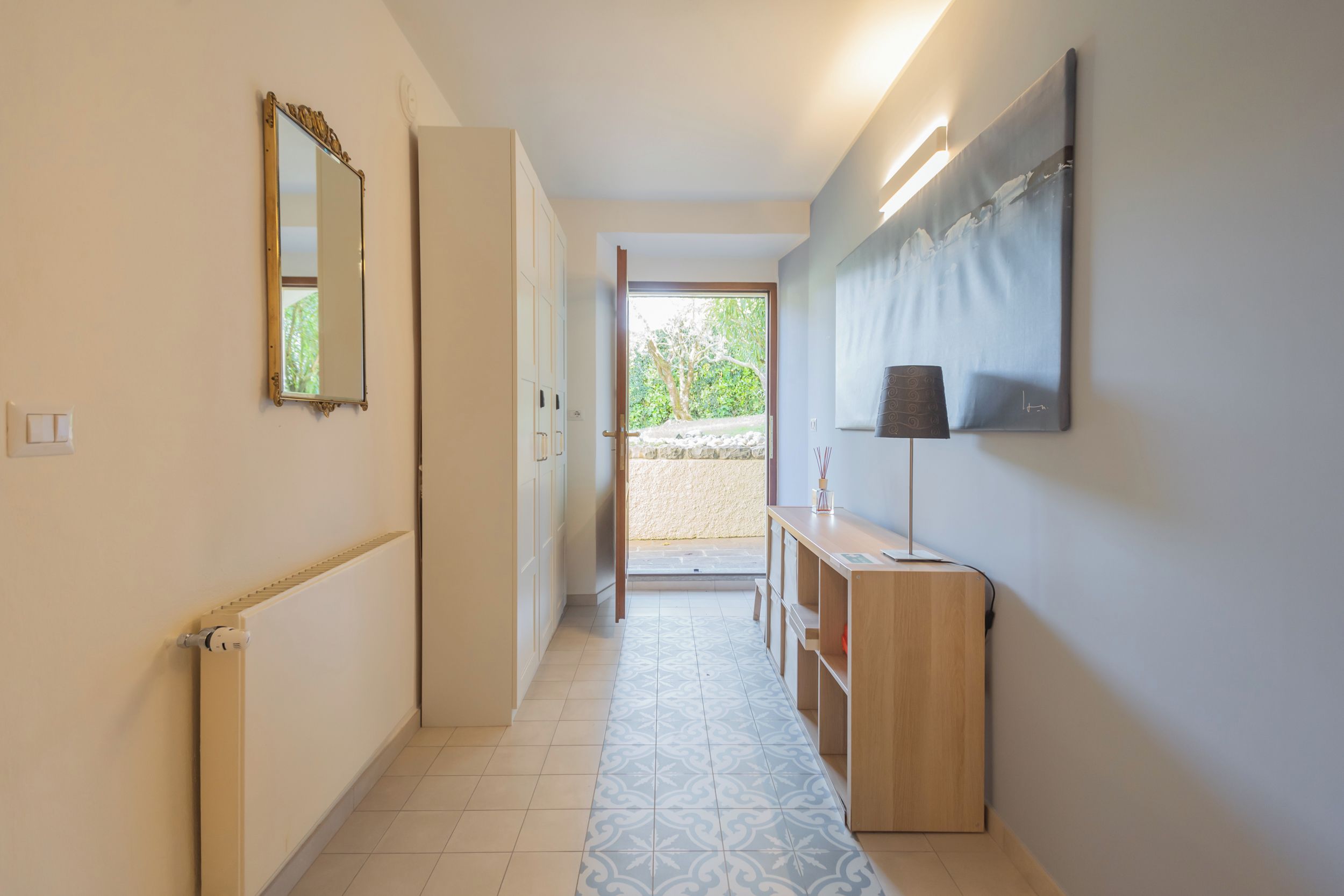 A hallway with a radiator, a mirror, a wooden console, and a door leading outside.