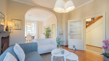 Una sala de estar con un sofá gris, una mesa de centro blanca y una puerta blanca que da a una escalera.