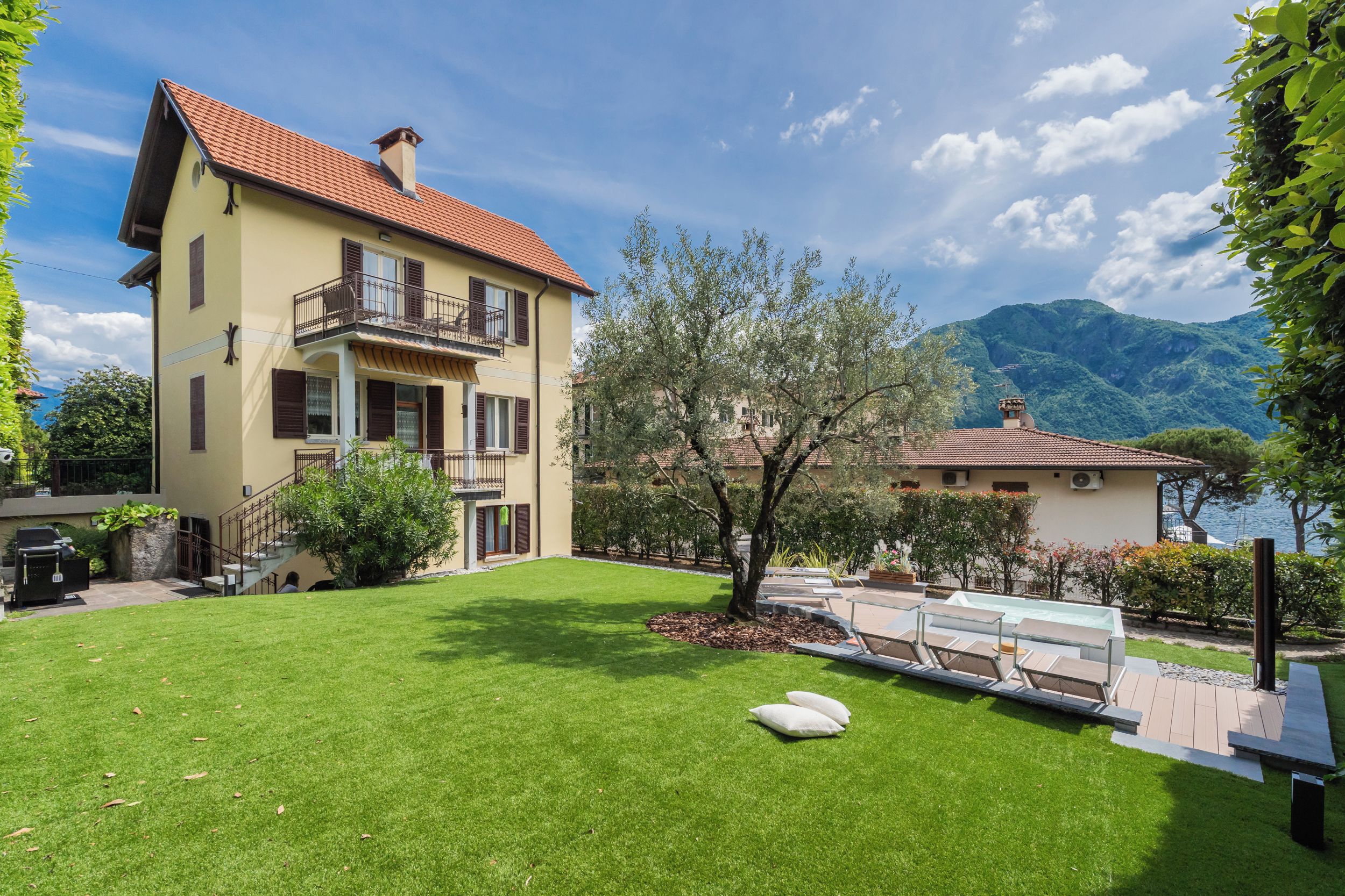 A two-story house with a balcony, a lawn, and a view of mountains.