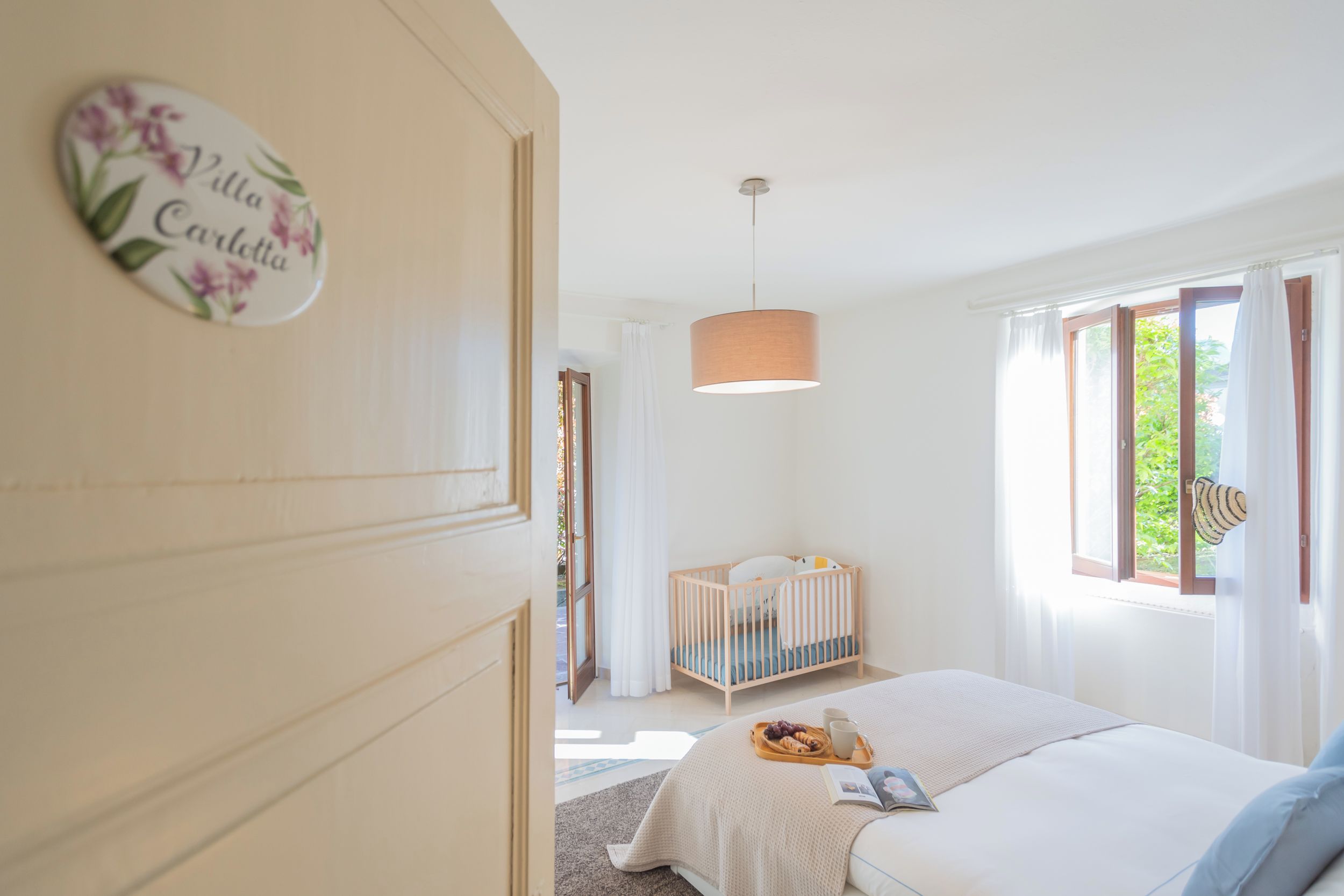 A bedroom with a crib, a bedside table with a tray of food, and a window with curtains.