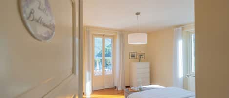 Een slaapkamer met een bed, nachtkastje, kaptafel, hanglamp en een deur die uitkomt op een balkon.
