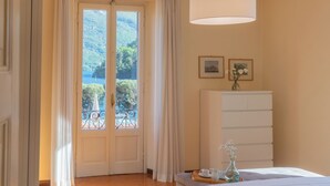 A bedroom with a large window, a bed, a dresser, and a bedside table with a vase of flowers. - Villa Ida by Rent all Como (Tremezzina)