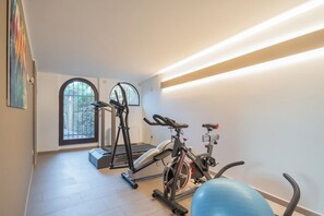 Ein Heimfitnessraum mit Trainingsgeräten, darunter ein Laufband, ein Ergometer und ein Gymnastikball.