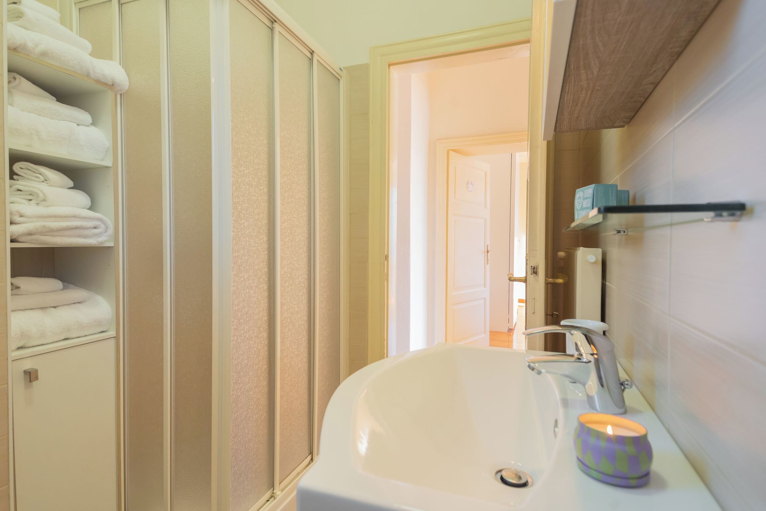 A bathroom with a white sink, a mirror, and a shelf with folded towels.