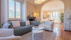 A living room with a sofa, armchairs, a coffee table, and a fireplace. There are large windows and a view of the outdoors. - Villa Ida by Rent all Como (Tremezzina)