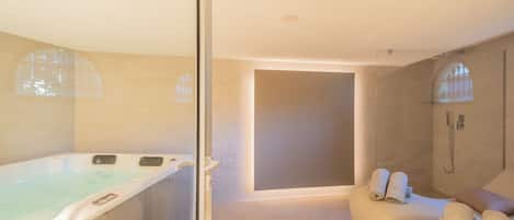 Un baño moderno con bañera de hidromasaje, ducha a ras de suelo y zona de estar con toallas.