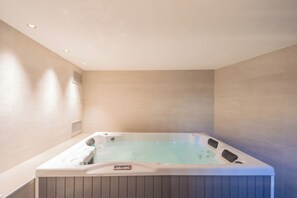 A modern bathroom with a large, rectangular hot tub, a control panel on the tub, and a wooden panel design on the lower half. - Villa Ida by Rent all Como (Tremezzina)