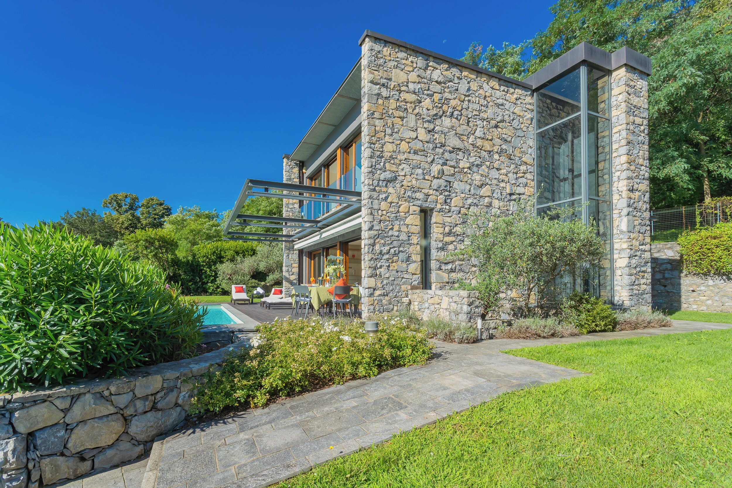 A modern house with stone exterior walls, a glass door, and a visible outdoor seating area with tables and chairs.