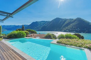 Una piscina con cubierta de madera, rodeada de abundante vegetación y vistas a montañas y un lago.