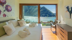 Ein Schlafzimmer mit einem großen Bett, einem Schreibtisch und Blick auf eine Berglandschaft und Wasser.