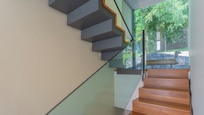 A modern staircase with glass railings and wooden steps, leading to an outdoor area with a stone bench and greenery. - Villa Infinity by Rent all Como (Como)