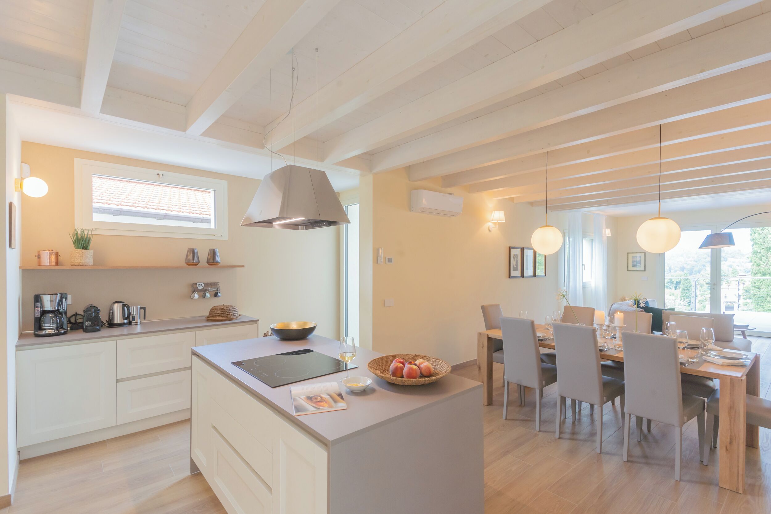 Une cuisine moderne avec des meubles blancs, un îlot central et un coin repas comprenant une table et des chaises en bois.