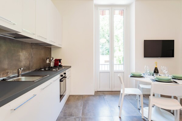 Una cocina moderna con armarios blancos, encimera negra y un comedor con una mesa blanca dispuesta para dos.