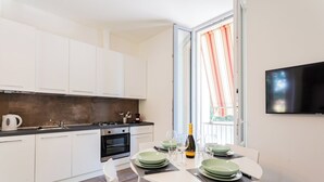 Una cocina moderna con armarios blancos, una mesa de comedor con platos verdes y un televisor montado en la pared.
