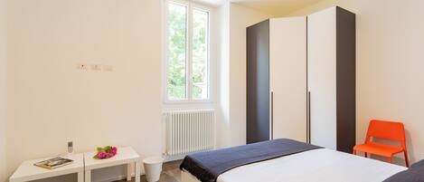 A bedroom with a bed, a small desk, a chair, and a radiator.