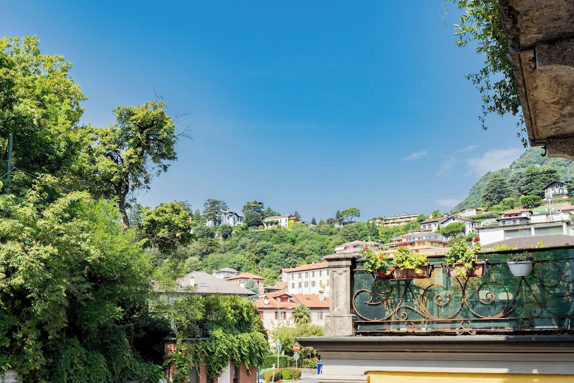 A residential area with houses on a hillside, a stone fountain with a sign, and lush greenery.