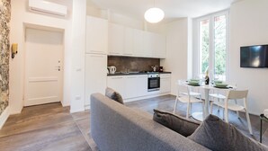 Una cocina moderna con armarios blancos, una mesa de comedor con sillas y un sofá gris.