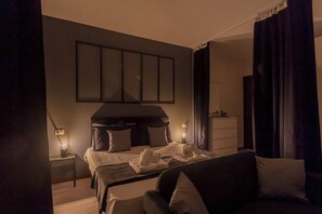 A dimly lit hotel room with a bed, a sofa, and a nightstand with a lamp. - Black Loft Como by Rent all Como (Como)