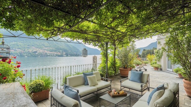 Eine Terrasse mit Sitzgelegenheit im Freien, Kübelpflanzen und Blick auf einen See und Berge.