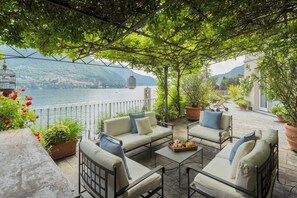 Una terraza con mobiliario exterior, plantas en macetas y vistas a un lago y montañas.